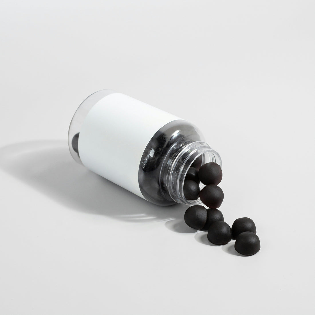 Black NMN supplement capsules spilling from a white bottle — Bio-Sync longevity supplements UK