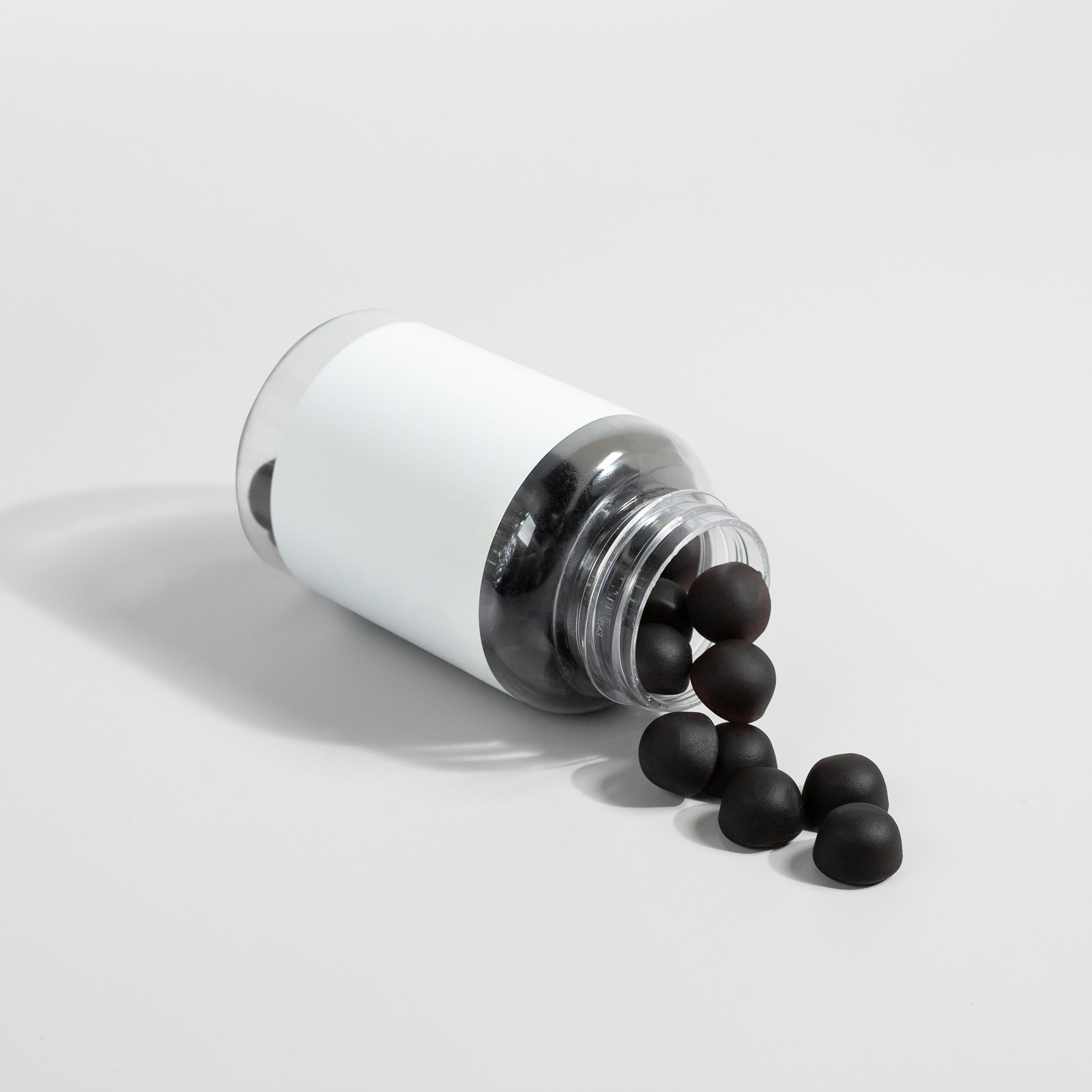 Black NMN supplement capsules spilling from a white bottle — Bio-Sync longevity supplements UK